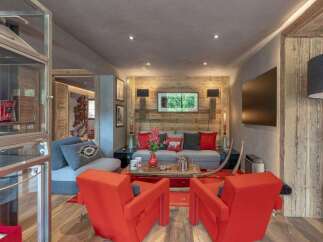 Experience luxurious mountain living in this stunning chalet living room, featuring a cozy grey sofa adorned with vibrant red and patterned throw pillows, complemented by two striking orange armchairs.