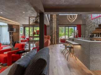 Experience luxury living in this stunning modern chalet, featuring a spacious open-plan living area with vibrant red armchairs and a sleek granite kitchen island.