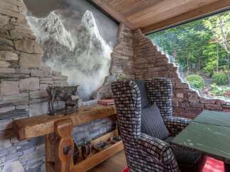 Experience rustic charm with this unique stone-clad seating area, featuring a striking mountain mural and a comfortable armchair.