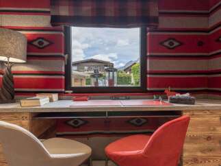 This cozy home office features a unique Southwestern-inspired decor with bold red and grey striped walls and a rustic wooden desk.
