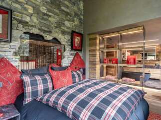 Experience rustic luxury in this unique bedroom featuring a striking stone wall and a cozy plaid bedding ensemble.