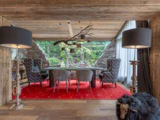 Experience rustic luxury in this stunning dining room, featuring a dramatic branch chandelier and a large window overlooking a lush garden.