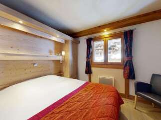 Experience cozy mountain living in this charming bedroom featuring a comfortable bed adorned with a vibrant orange quilted throw.