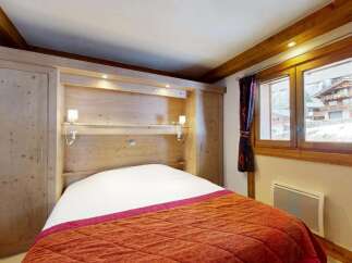 Experience cozy mountain living in this charming bedroom featuring a built-in wooden wardrobe and a comfortable bed adorned with a vibrant orange quilt.