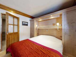 Experience cozy alpine living in this charming bedroom featuring a warm wooden interior and a plush bed adorned with a vibrant orange and pink comforter.