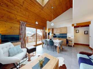 Experience cozy living in this charming mountain chalet, featuring a spacious open-plan living area with a rustic wooden ceiling and a modern kitchen.