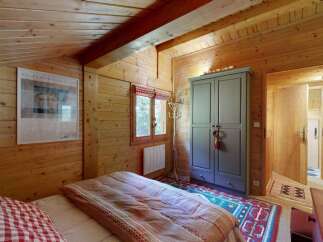Experience rustic charm in this cozy wooden cabin bedroom, featuring a comfortable bed with plaid accents and a large wardrobe for ample storage.