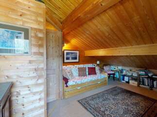 Cozy attic room with warm wood paneling and a sloped ceiling, featuring a comfortable daybed adorned with decorative pillows.