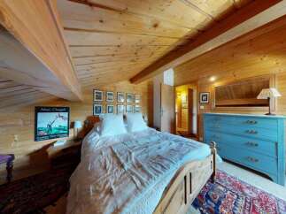 Experience rustic charm in this cozy attic bedroom, featuring exposed wooden beams and walls that create a warm, inviting atmosphere.