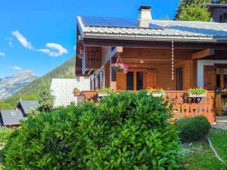 Experience alpine living in this charming wooden chalet, featuring a spacious balcony adorned with flower boxes and a hanging basket, perfect for enjoying mountain views.