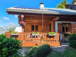 Experience breathtaking mountain views from this charming wooden chalet, featuring a spacious balcony adorned with flower boxes and intricate railings.
