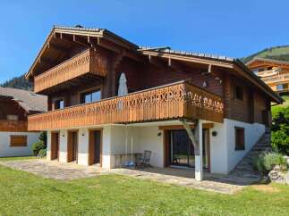 Experience alpine living in this charming wooden chalet, featuring intricate balcony railings and a spacious patio perfect for enjoying mountain views.