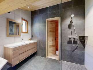 Experience modern alpine living in this stunning bathroom featuring a sleek wooden vanity and a spacious walk-in shower with dark stone tiles.