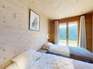 Experience serene mountain living in this charming bedroom featuring cozy twin beds and a stunning view through the large glass doors.