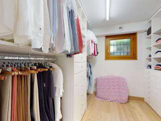 Discover this spacious walk-in closet, meticulously organized with ample hanging space for shirts and trousers, complemented by a dedicated shelving unit for folded clothes.