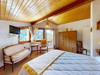 Experience cozy mountain living in this charming bedroom featuring a comfortable bed, a quaint seating area, and a large wooden wardrobe for ample storage.