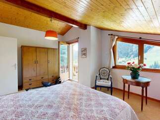 Experience breathtaking mountain views from this charming bedroom, featuring a cozy bed, a spacious wooden wardrobe, and a private balcony accessible through French doors.