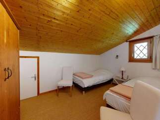 This charming attic bedroom features a cozy wooden ceiling and a quaint diamond-paned window, offering a unique and inviting atmosphere.