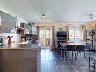 This modern open-plan living space features a sleek grey kitchen with ample cabinet storage and a microwave, adjacent to a dining area with a glass-top table and chairs.