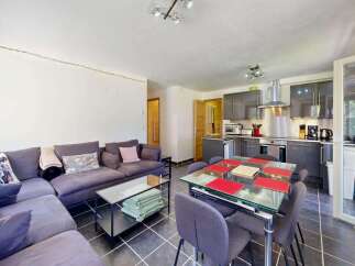 This open-plan living and dining area features a spacious L-shaped sofa perfect for relaxation, complemented by a modern dining set with glass tabletop and comfortable seating.