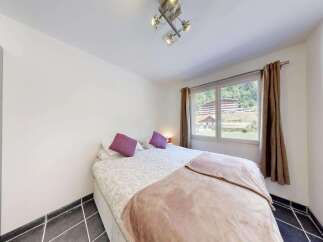 This charming bedroom features a comfortable double bed adorned with plush purple pillows and a soft, textured throw blanket.