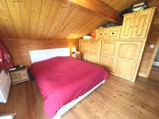 Experience cozy living in this charming attic bedroom, featuring a comfortable bed with a plush red comforter and a stylish white headboard.