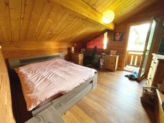 Experience cozy living in this charming wooden cabin bedroom, featuring a comfortable bed with pink linens and a spacious desk area perfect for work or study.