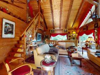 Experience rustic charm in this cozy wooden cabin living room, featuring a grand fireplace, comfortable seating, and a beautiful staircase.