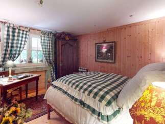 Charming rustic bedroom featuring a cozy bed with a green and white gingham comforter, complemented by wooden paneled walls and a vintage armoire.