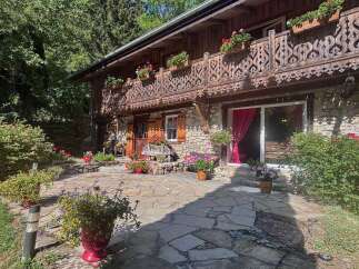 Charming stone and wood chalet nestled amidst lush greenery, featuring a picturesque balcony with intricate carvings and abundant flower boxes.