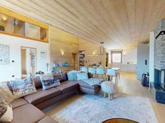 Experience luxurious mountain living in this stunning chalet featuring a spacious open-plan living area with a modern stone fireplace and a large sectional sofa.