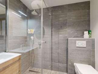Experience modern luxury in this beautifully appointed bathroom, featuring a spacious walk-in shower with sleek grey tiling and a convenient handheld showerhead.