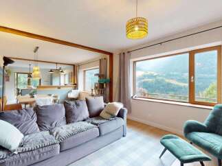 Experience breathtaking mountain views from this stunning living room, featuring a plush grey sofa and a comfortable teal armchair with an ottoman.