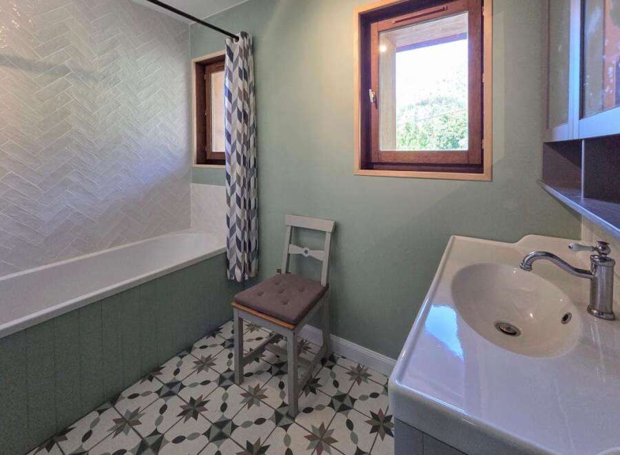 This charming bathroom features a classic white bathtub with a herringbone tile backsplash, complemented by a decorative patterned floor.