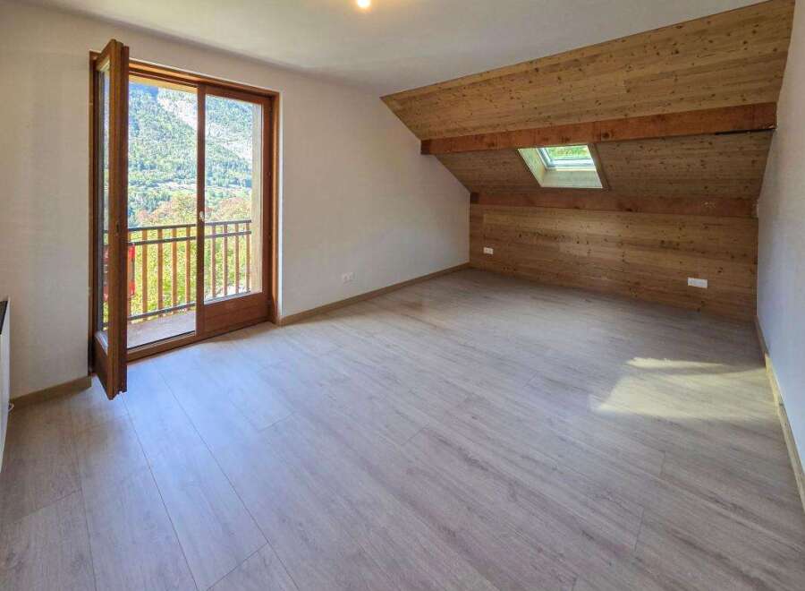 This spacious attic room features a beautiful wooden-paneled sloped ceiling with a skylight, offering natural light and a cozy ambiance.