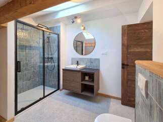 This modern bathroom features a sleek walk-in shower with grey tiled walls and a black frame.