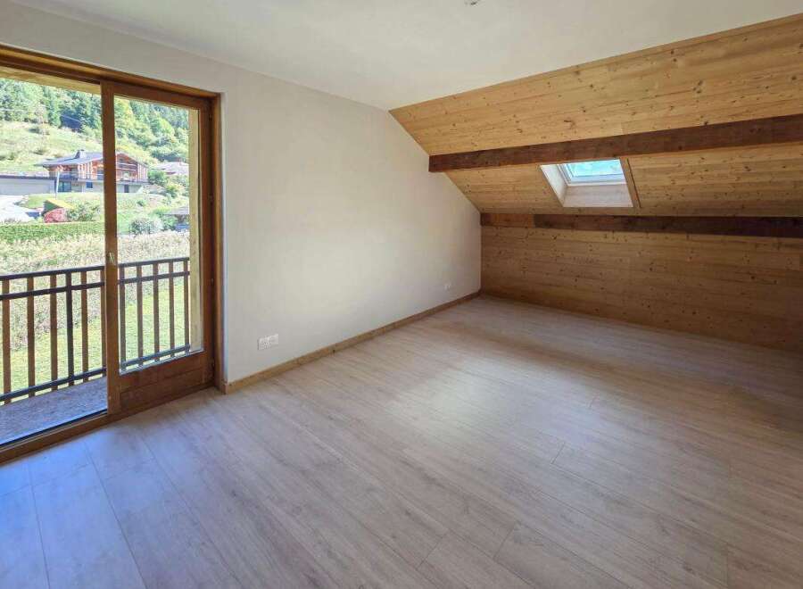 Experience breathtaking mountain views from this charming attic bedroom, featuring a private balcony and a cozy, wood-paneled ceiling with a skylight.
