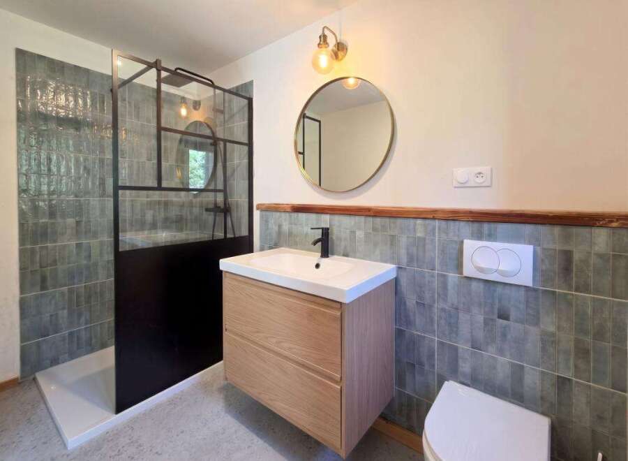 This modern bathroom features a sleek walk-in shower with a black metal frame and textured grey tiles.