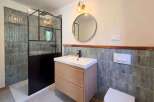 This modern bathroom features a sleek walk-in shower with a black metal frame and textured grey tiles.