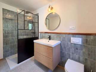 This modern bathroom features a sleek walk-in shower with a black metal frame and textured grey tiles.
