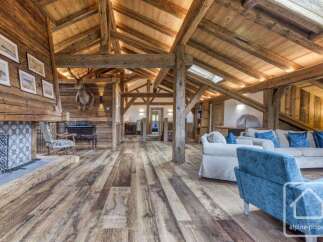 Experience rustic luxury in this stunning chalet living room, featuring exposed wooden beams, a grand stone fireplace, and a majestic taxidermied deer head.