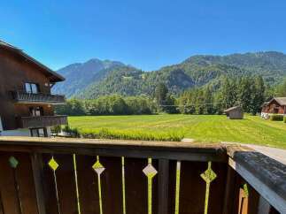 Experience serene mountain living from this charming property, featuring a traditional wooden exterior and balconies offering breathtaking views of lush green fields and majestic peaks.