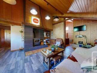 Experience rustic charm in this cozy living room, featuring a striking stone fireplace with a wood-burning stove and exposed wooden beams.