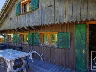 Experience rustic charm with this wooden cabin featuring traditional green shutters and a welcoming outdoor dining area.