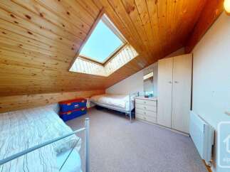 This charming attic bedroom features a unique sloped wooden ceiling and a large skylight that floods the space with natural light.