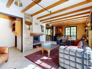 Experience rustic charm in this inviting living room, featuring a grand stone fireplace and exposed wooden beams that create a warm, cozy atmosphere.