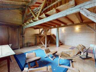 Experience rustic charm in this unique wooden interior, featuring exposed beams and a lofted space accessible by stairs.