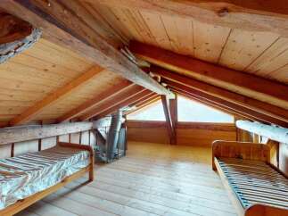 Discover this charming attic bedroom featuring rustic wooden beams and a sloped ceiling, creating a cozy and unique atmosphere.