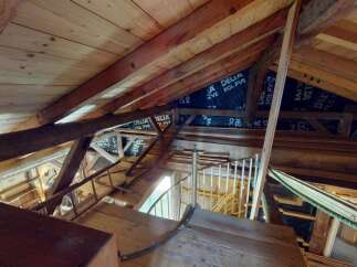 Explore the intricate wooden beams and rustic charm of this attic space, showcasing exposed rafters and a unique spiral staircase.