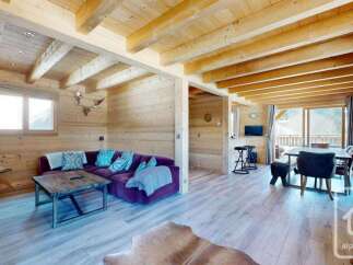 Experience cozy living in this charming wooden chalet, featuring a plush purple sofa and a rustic coffee table perfect for relaxing evenings.